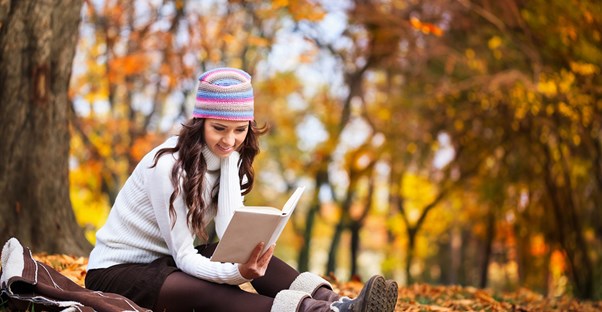 Young woman reading a book outside in the fall weather