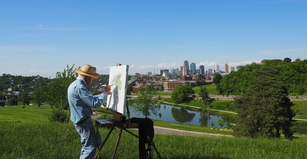 a retired man painting a landscape in front of a city skyline
