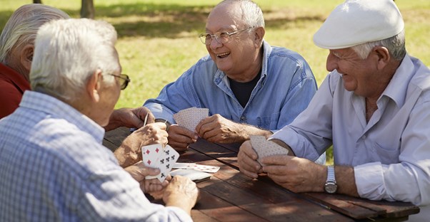 Elderly men play cards and discuss their senior care options.