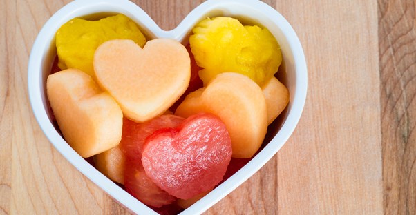 A heart shaped bowl full of fruit given to a kid as a snack.