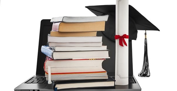 A degree sits on top of a laptop along with a stack of books