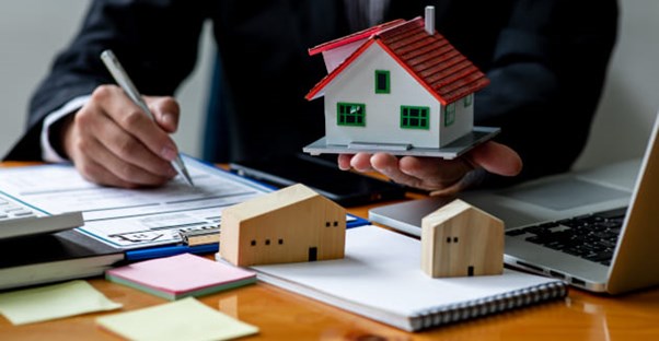 A person holding a small house and signing rental paper