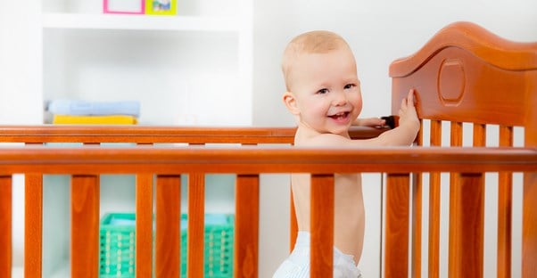 a baby laughs while standing in a crib