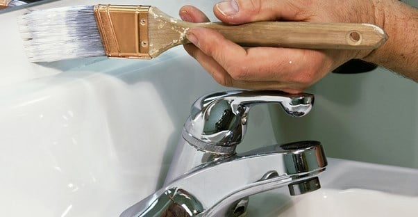 a paintbrush being used to paint a wall above a sink and below a bathroom mirror