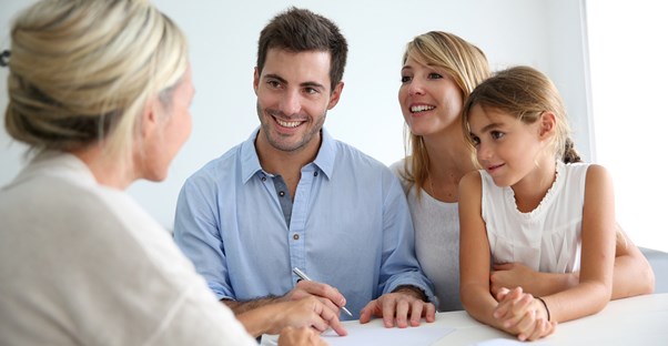 Real estate agent points out something on the paper as young family smiles back