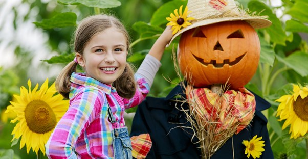 Little girl poses next to a scarecrow in her yard