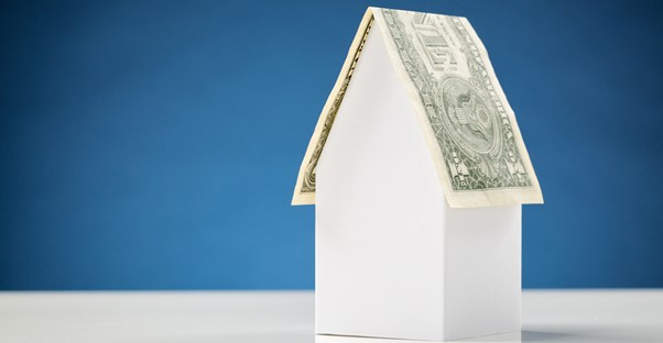 A paper house with a roof made out of money to symbolize that roofing can cost you.