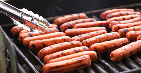 Hot dogs cooking on a grill at a tailgate.