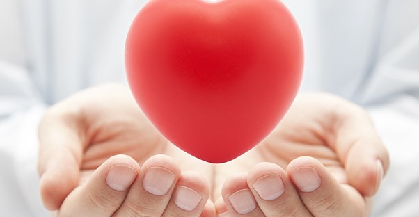 Two white hands cupped underneath a floating, red heart that is glowing with happiness from having health insurance