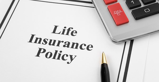 a printed life insurance policy booklet under a calculator and a pen showing that it is important to review policies before choosing the right one for you