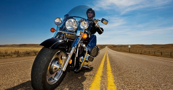 a man rides a motorcycle down a deserted 2-lane highway