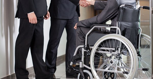 Man in wheelchair shaking hands with two men in suits