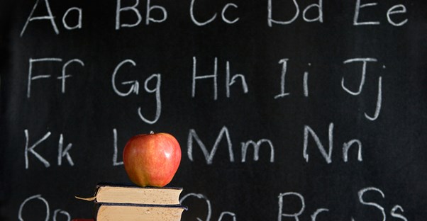 An apple on a stack of books on a desk in front of a chalkboard