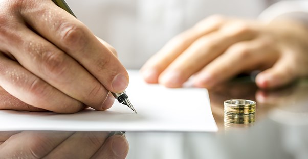 man writing on divorce legal document with wedding ring sitting on the table