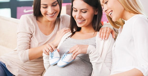 mom holding baby shoes with friends at baby shower