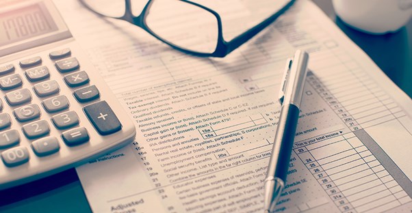 A tax return document laying on a desk with some glasses, a calculator, and a pen