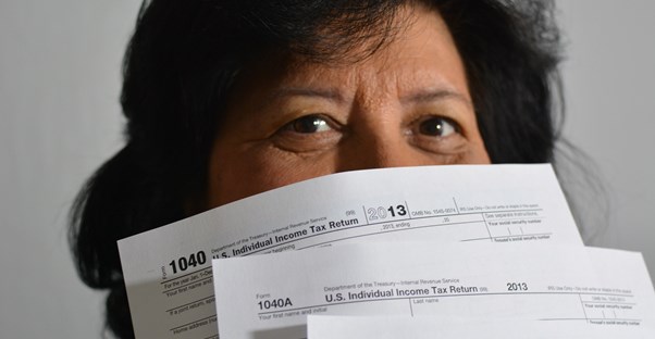 a woman holds tax filing forms in front of her face so only her eyes are showing