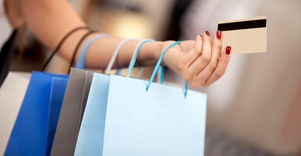 Woman holding out a credit card with shopping bags containing worthwhile splurges lined up on her arm
