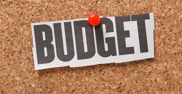 Piece of paper reading Budget tacked to a cork board to remind you to create a budget.
