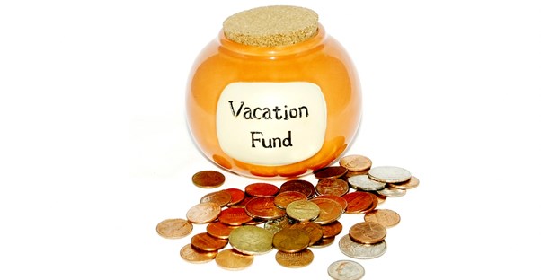 A yellow jar that says Vacation Fund with a pile of spare change around it that is being budgeted for a trip.