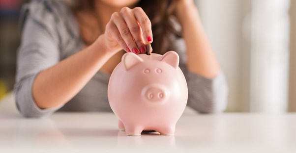 A new college grad smiles as she places the money she saves for the future into her childhood piggy bank