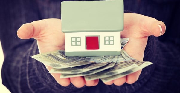 Woman holding a toy house and a fan of dollars bills in the palms of her hands to represent how home loans work.