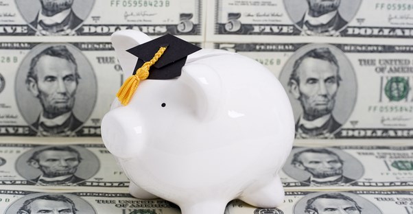 A piggy bank wearing a graduation hat in front of money that was received through financial aid.