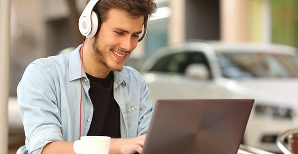 Man wearing headphones sitting at cafe on laptop computer