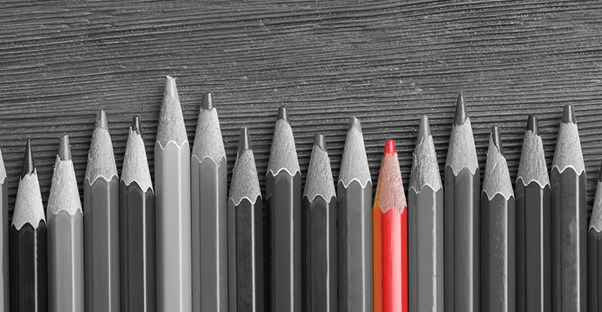 black and white photo of pencils lined up on a special education teacher's desk, with one pencil colored in red. 