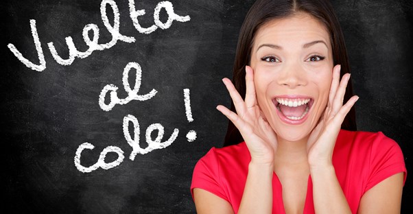 Girl flashes a huge smile while standing in front of a chalkboard with spanish written on it