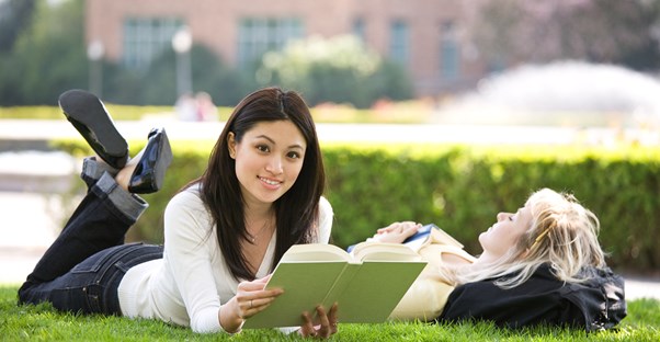 Two college students lie on the grass and read their textbooks