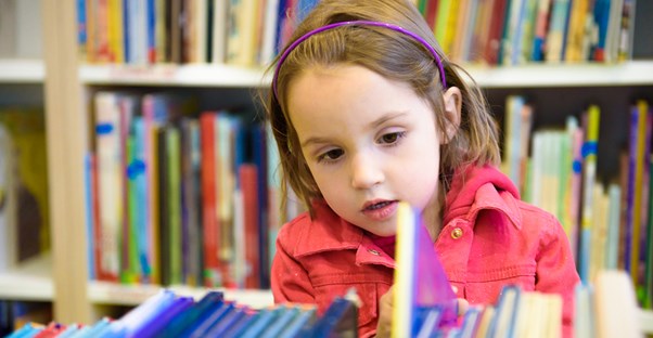 A young preschooler looks through books in the school library