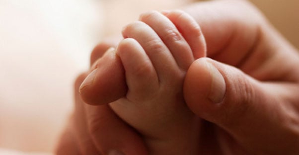A close up of a baby's hand grasping the hand of its father.