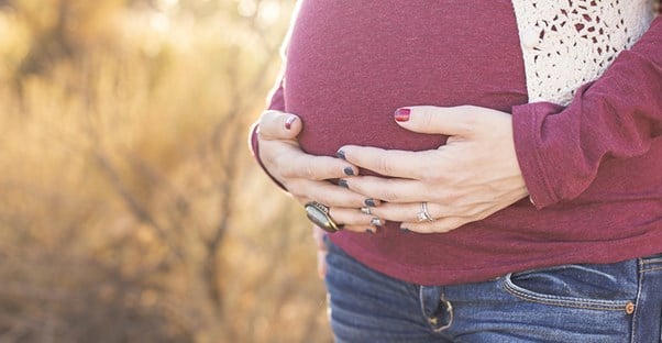 A close up of a woman holding her hands together around her pregnant belly.