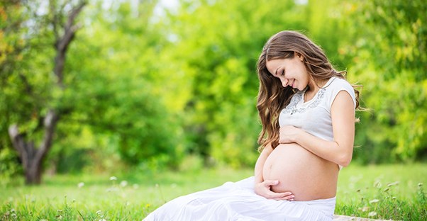 a woman sits in a field holding and looking at her pregnant stomach