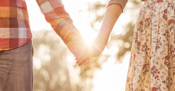 a couple holds hands on a date in front of a sun flare