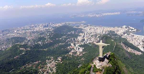 a mountain top view looking down at Rio de Janiero with the Christ the Redeemer statue in the foreground