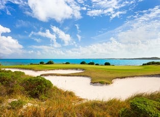 a sand bunker next to a golf green with the ocean in the background