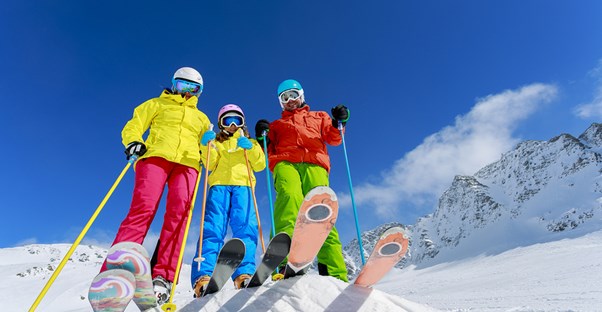 a family of skiers stands at the top of a run about to ski down