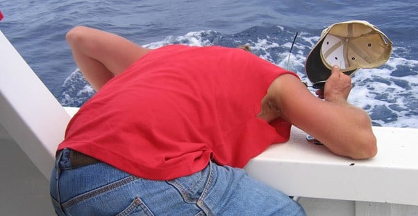 A man bends over the side of a boat while suffering from sea sickness.