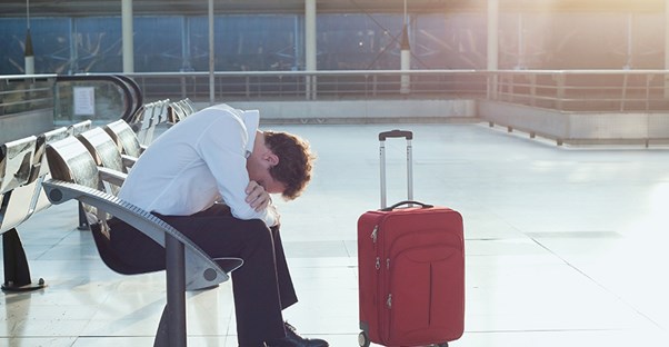 A man sits in a terminal with his head in his arms exasperated and tired.