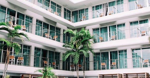 A retro styled hotel has chairs on the balconies and a large palm tree in the courtyard.