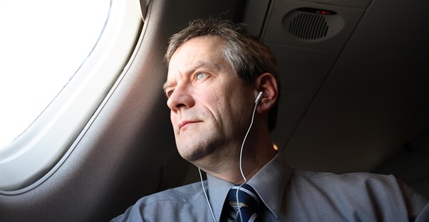 a business man gazes out of a business class airplane window while listening to music through headphones
