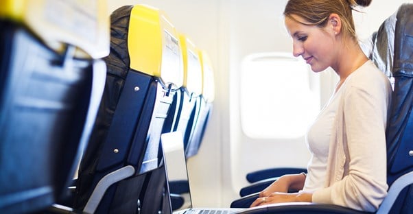 a woman sits in economy class typing on her laptop