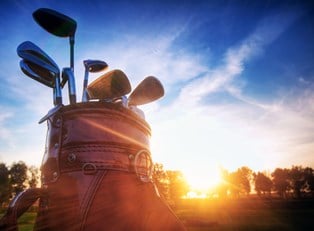 a close up of a golf bag with golf clubs sticking out of the top and the sun setting behind it