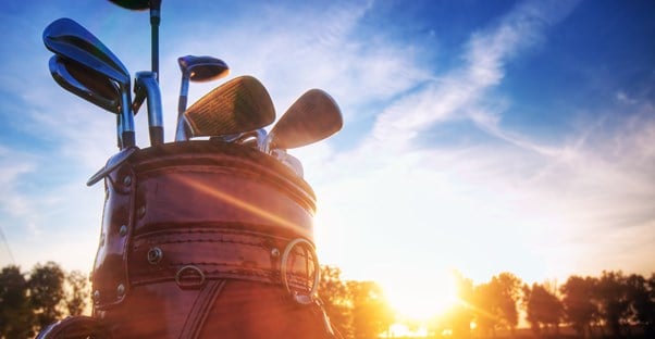 a close up of a golf bag with golf clubs sticking out of the top and the sun setting behind it