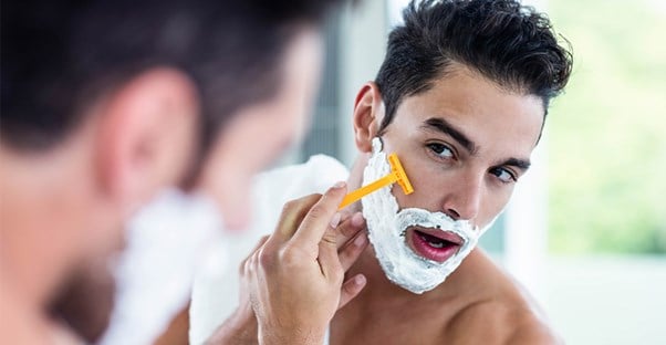 A guy shaves in the mirror